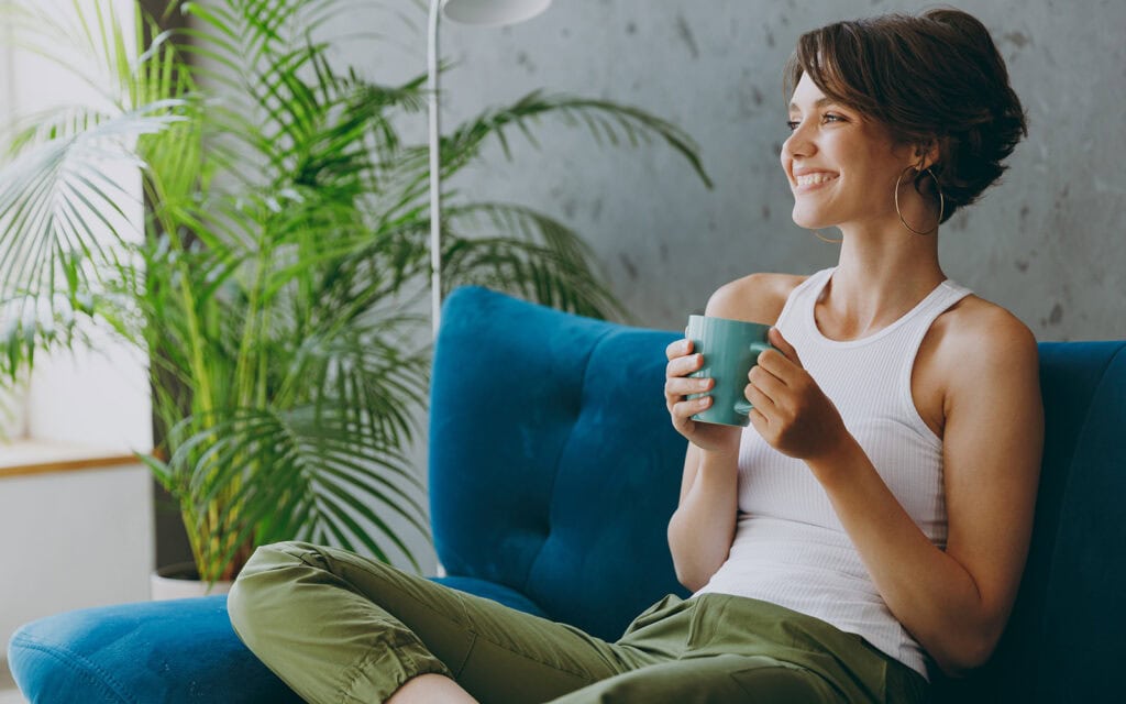 a woman smiling on her couch having coffee